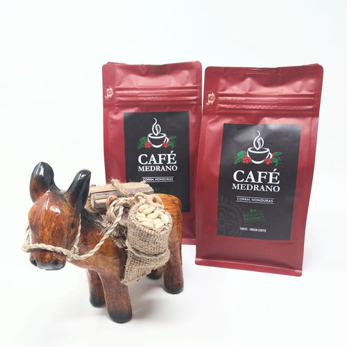 Two red coffee bags with 'Café Medrano' branding and a wooden donkey figure on a white background.