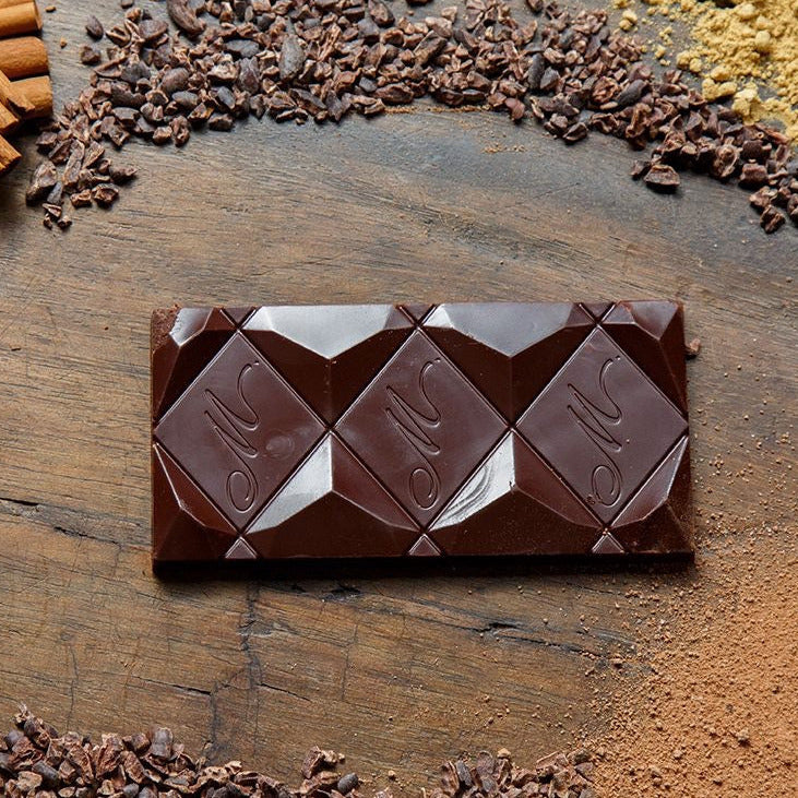 Chocolate bar with McCormick logo on a wooden surface with cocoa beans and cinnamon sticks.