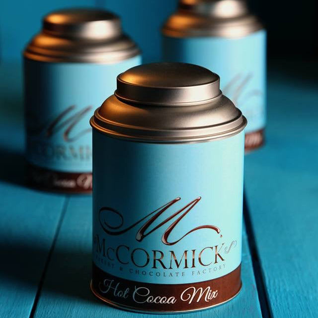 Three cans of McCormick hot cocoa mix on a blue wooden surface